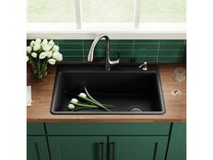 a black kitchen sink with flowers on the counter and green tile behind it, in front of a window