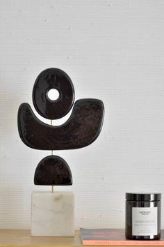 a black sculpture sitting on top of a wooden table next to a jar of cream