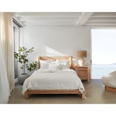 a bedroom with a bed, nightstands and large window overlooking the ocean is pictured in this image