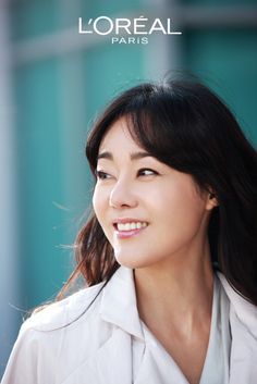 a woman with long dark hair and white shirt smiling at the camera while standing in front of a building