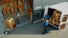 two men unloading boxes from the back of a white truck in a warehouse with pallets