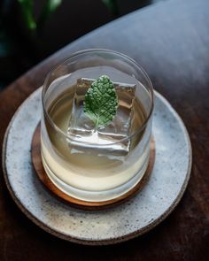 a glass filled with liquid on top of a wooden table next to a green leaf