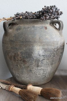 an old vase with some black berries on it and a broom sitting next to it