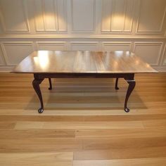 a wooden table sitting on top of a hard wood floor next to a white wall