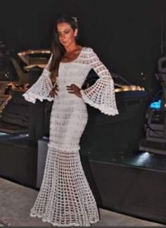 a woman standing on top of a boat in a long white dress with bell sleeves