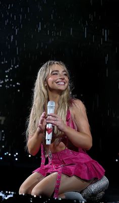 a woman sitting on the ground holding a microphone in front of her face and smiling