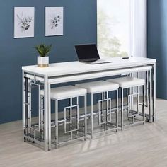 a white table with four stools and a laptop on it in front of a blue wall