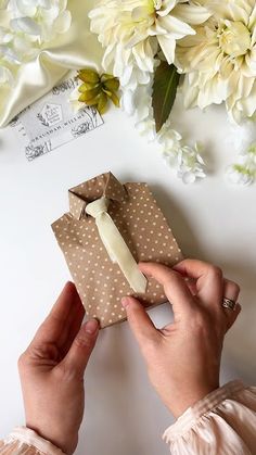 a person holding a piece of paper with a tie on it next to some flowers