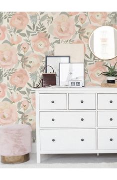 a white dresser sitting next to a wall with flowers on it and a mirror above it