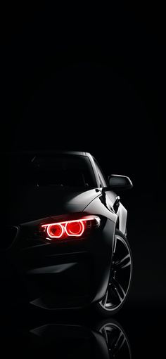 the back end of a black sports car with its lights turned on in the dark