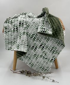 a green and white blanket sitting on top of a wooden chair next to a plant