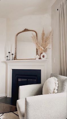 a living room with white furniture and a mirror on the fireplace mantel above it