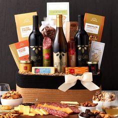 a basket filled with wine, cheese and crackers next to other snacks on a table