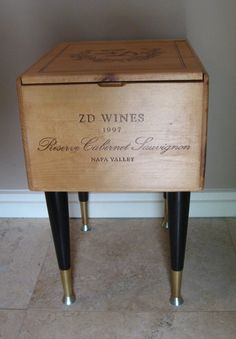 a wooden wine box sitting on top of two black metal legs in front of a wall