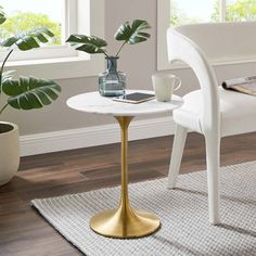 a white table with a gold base and a plant in the corner next to it