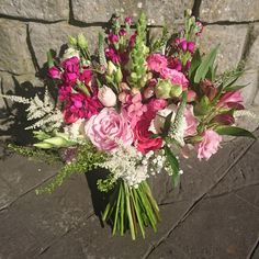 a bouquet of pink and white flowers sitting on top of a stone floor next to a brick wall