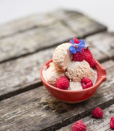 two scoops of ice cream and raspberries in a bowl on a wooden table