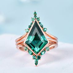 an emerald colored ring with green stones on the bottom and gold band, set against a light blue background