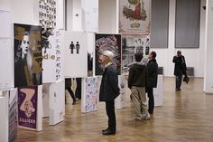 several people standing in an art gallery looking at posters