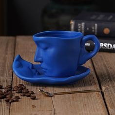 a blue coffee cup sitting on top of a wooden table next to some coffee beans