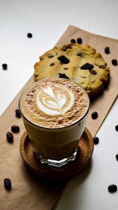 a cappuccino on a saucer next to a cookie and coffee beans