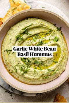 a white bowl filled with hummus and herbs on top of a marble table next to pita chips