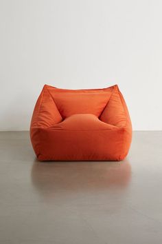 an orange bean bag chair sitting on top of a cement floor next to a white wall