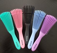 four different colored hair brushes sitting next to each other on top of a black table