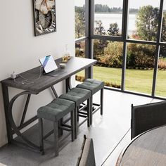 a table with two stools and a laptop on it in front of a large window