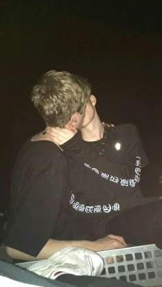 two young men sitting next to each other on a boat at night, one holding his neck around the other's shoulder