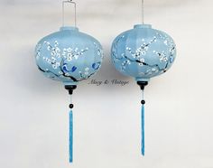 two blue lanterns with white flowers on them hanging from hooks, one has a string attached to it