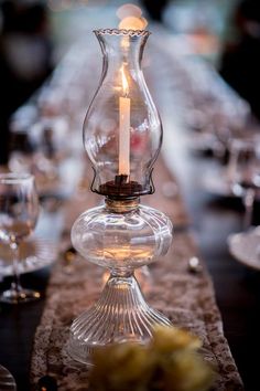 a candle is lit in a glass vase on a long table set with wine glasses