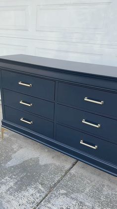 a large blue dresser with gold handles on the top and bottom, sitting in front of a garage door