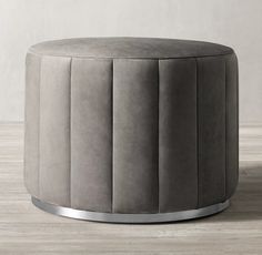 a round grey ottoman sitting on top of a wooden floor next to a white wall