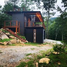 a small black cabin in the woods with stairs leading up to it's second floor