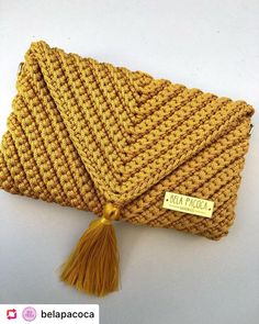 a yellow knitted purse with a tassell on the side and a tag hanging from it