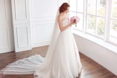 a woman in a wedding dress looking out the window with her bouquet on her hand