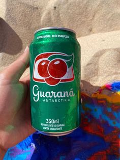 a hand holding a can of guarana on top of a colorful blanket in the sand