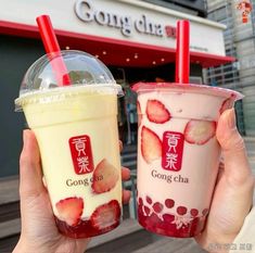 two people holding up drinks in front of a building with chinese writing on the side