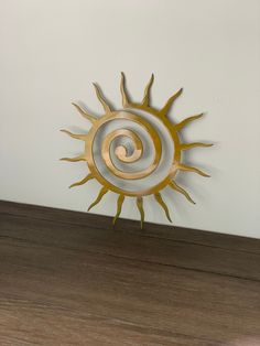 a metal sun sculpture sitting on top of a wooden floor next to a white wall