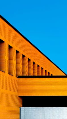 an orange building with a clock on the side of it's face and a blue sky in the background