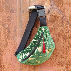 a green and white purse hanging on the side of a wall with a black strap