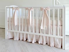 a baby crib with pink bedding and bows on the top, in a white room