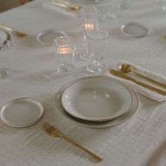 a table set with white plates and gold cutlery, silverware, and glasses