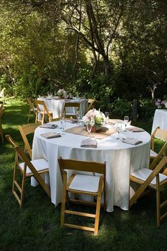 the table is set with white linens and wooden chairs