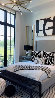 a large bed sitting next to a tall window in a room with black and white decor