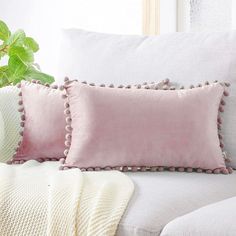 a white couch with two pillows and a blanket on it next to a potted plant