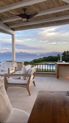 an outdoor living area with couches and tables on the balcony overlooking the ocean at dusk