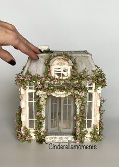 a hand is holding a doll house with flowers on it