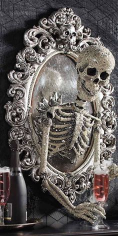 a skeleton sitting in front of a mirror with wine glasses on the table next to it